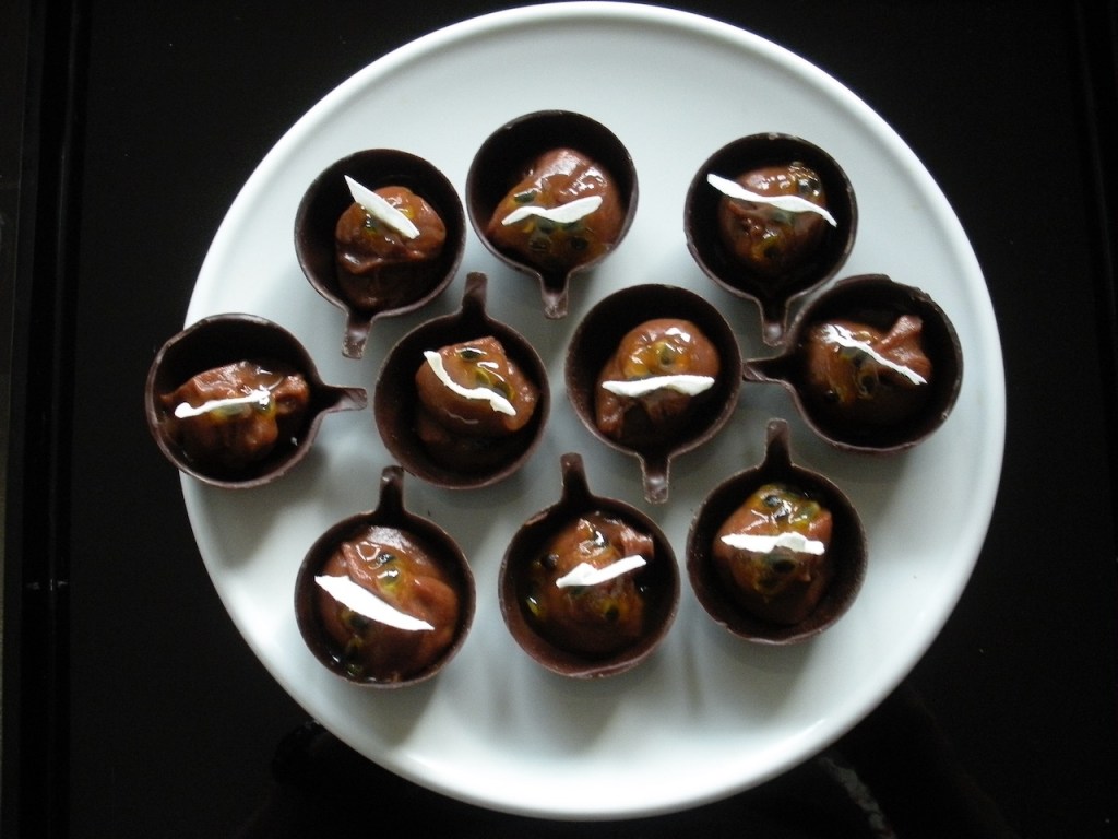 Little chocolate cups fills with a milk chocolate truffle, drizzled with passion fruit and garnished with a coconut flake.
