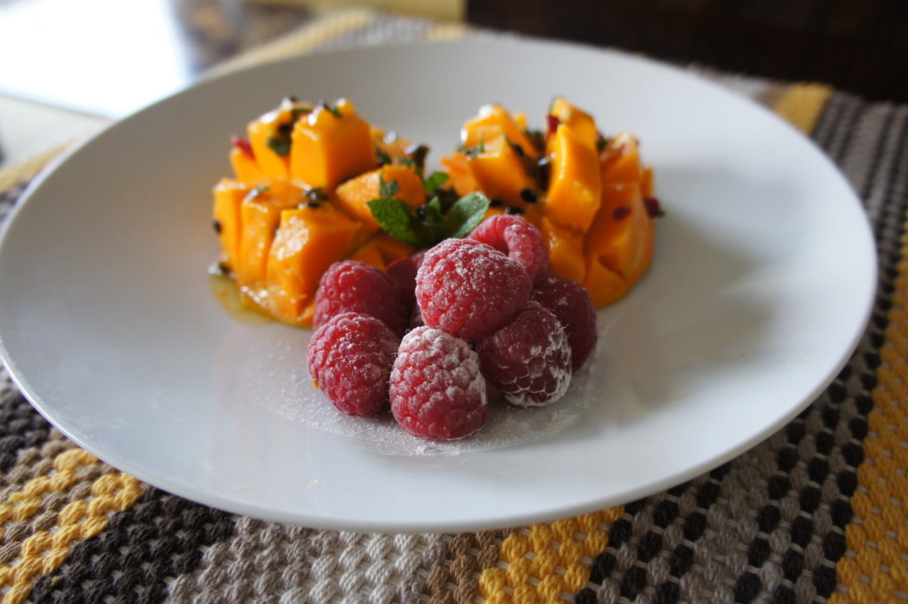A plate of cut mango, drizzled with passion fruit and served with raspberries.