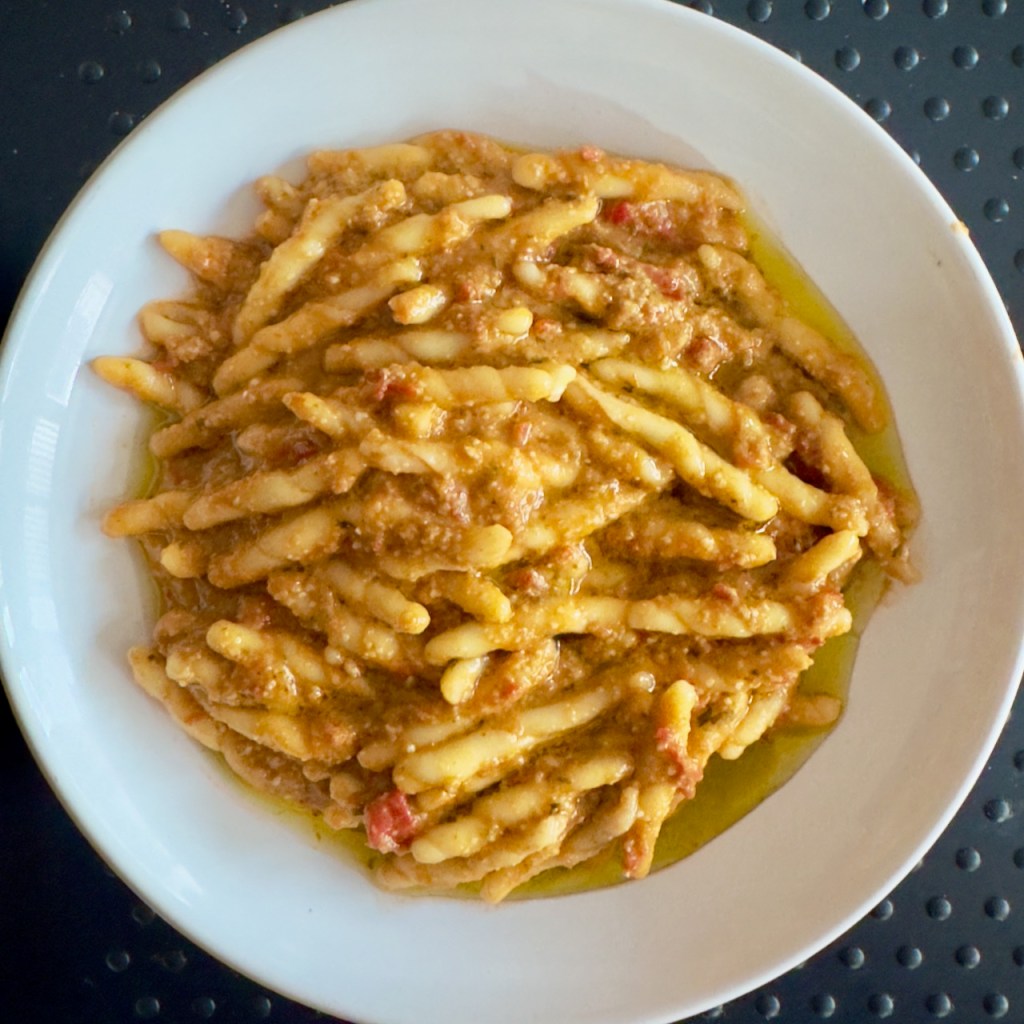 A dish of trofie pasta served with a cherry tomato and pesto sauce.